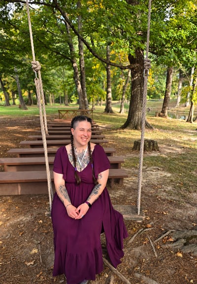 Cyndi, smiling on a rope swing among the trees, wearing a plum dress